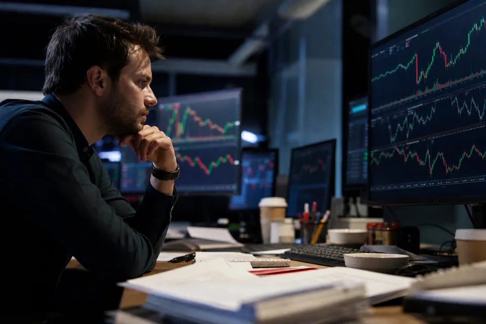 Trading screens with share price charts in a dim market room